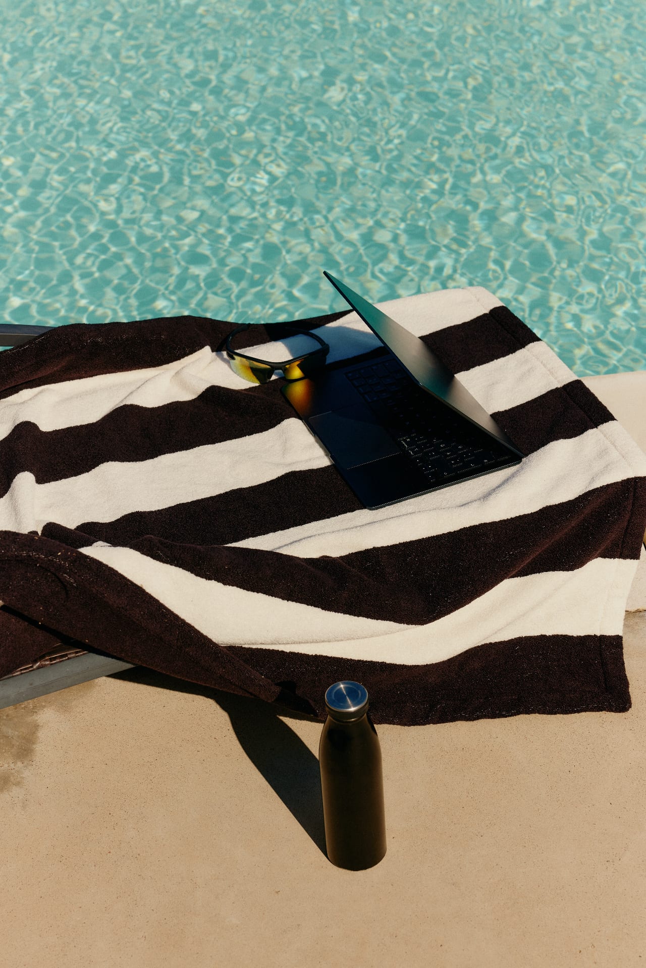 Laptop and sunglasses on a towel by the pool