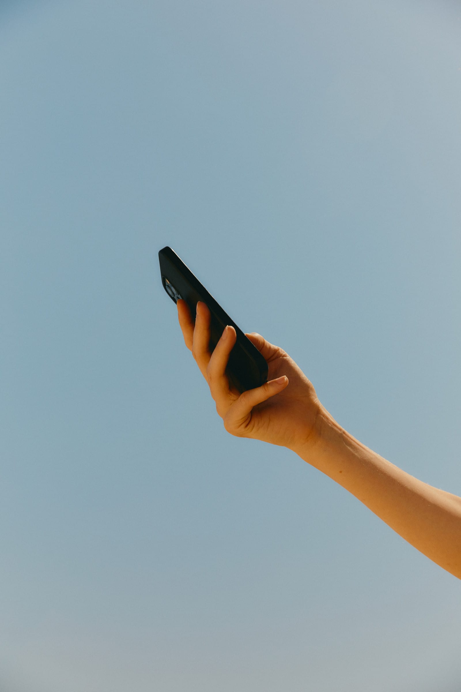 Hand holding a phone against a blue sky